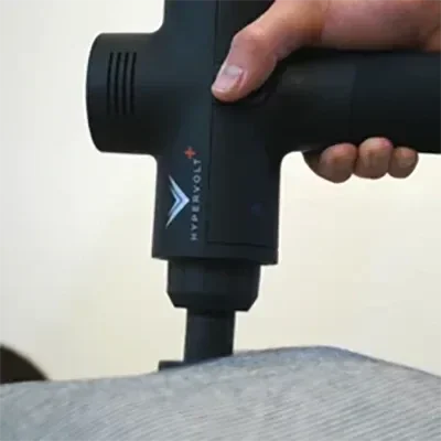 A practitioner using a hand-held percussion therapy device on a patient's back